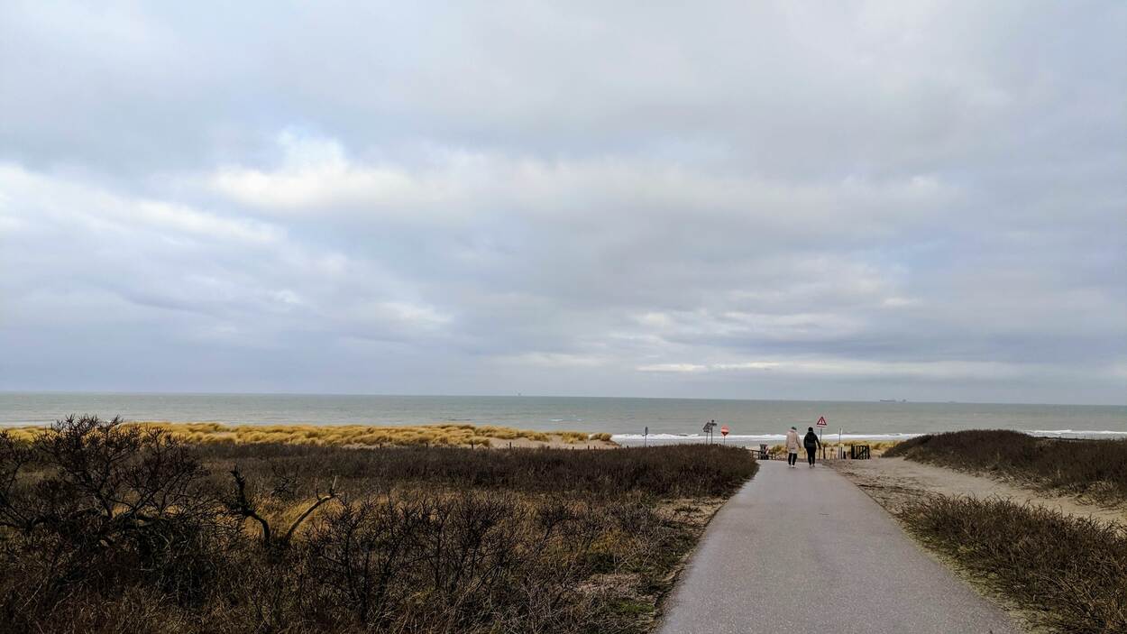 Twee mensen lopen door de duinen en de zee op de achtergrond