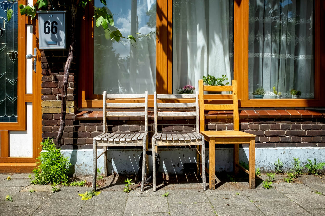 Voor een huis staan drie houten stoelen.
