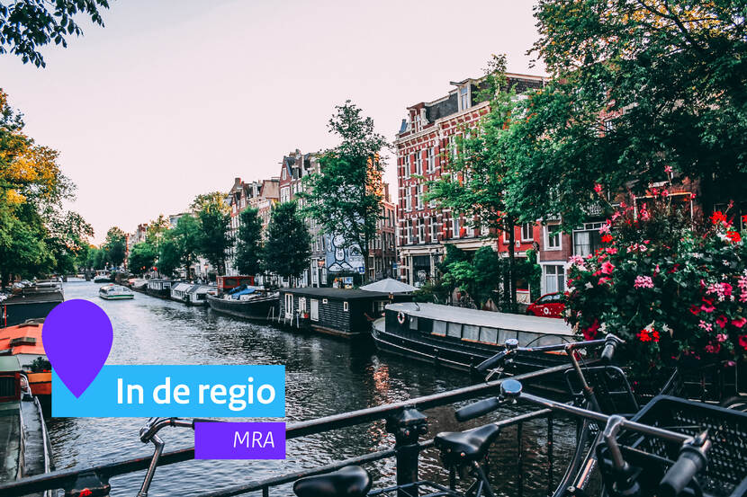 Een gracht in Amsterdam. Op de brug staan fietsen. Naast de gracht staan herenhuizen. Links onderin staat de tekst In de Regio. MRA