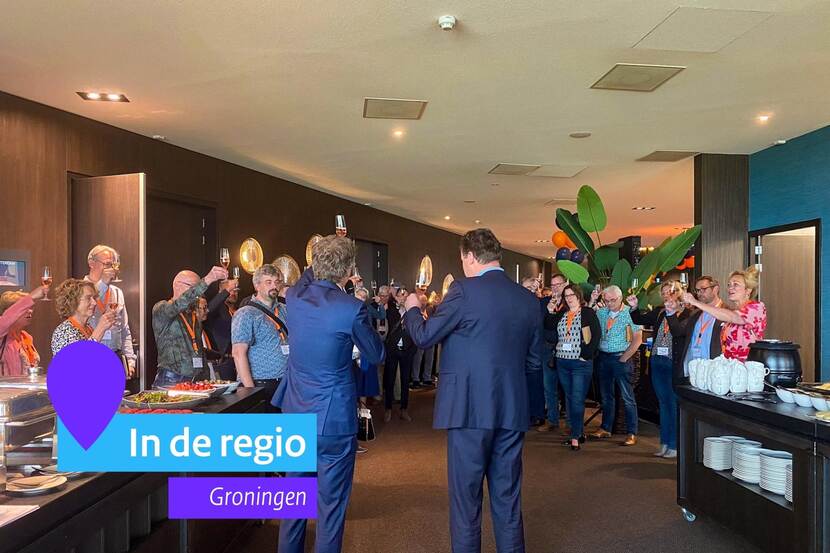 Aanwezigen op de Toogdag heffen het glas. Ze staan binnen.