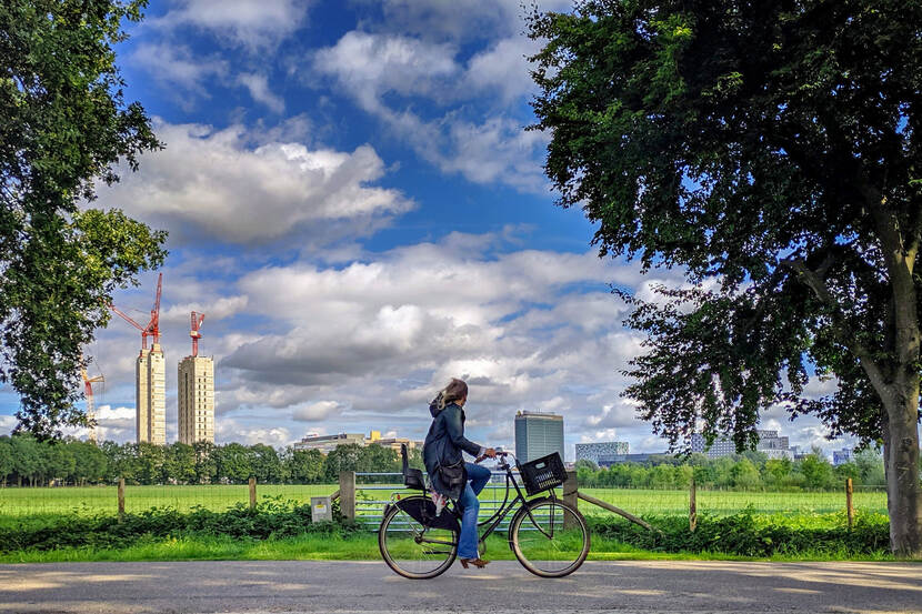 Foto van fietser in een landschap met de hoogbouw van de stad op de achtergrond