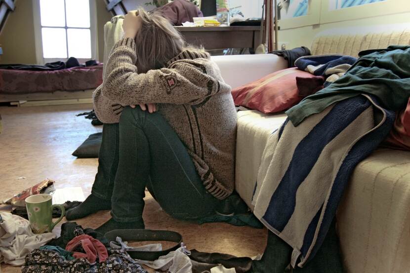 Een vrouw zit naast haar bed met de handen in het haar