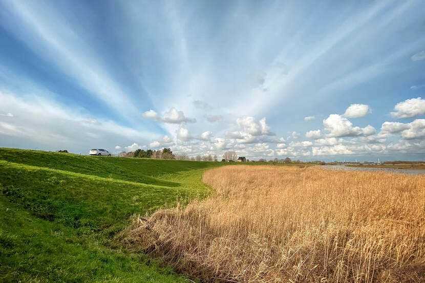 landschapsfoto met een dijkje, water en de zon