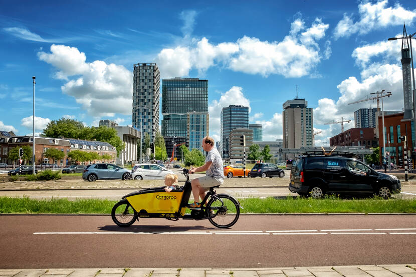 Een bakfietser op het fietspad met de weg en de skyline in de achtergrond