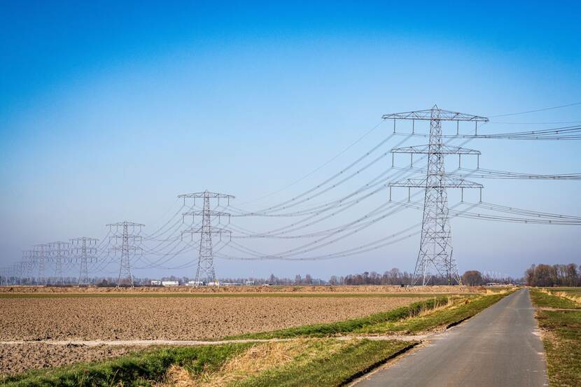 Veld met hoogspanningsmasten die over een smalle weg lopen