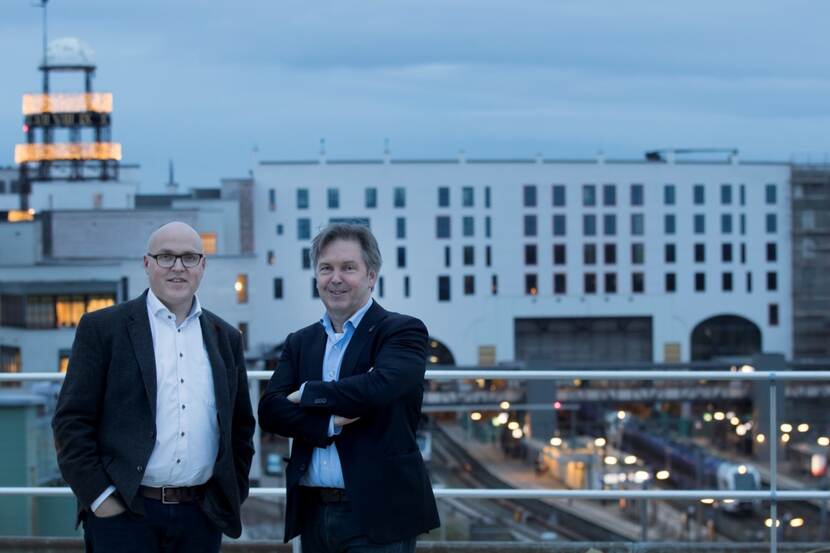 Peter Bertholet (rechts) en Charles Claessens (voorzitter commissie mobiliteit Parkstad Limburg) op het dak van het vroegere CBS-gebouw in Heerlen met op de achtergrond het nieuwe station.