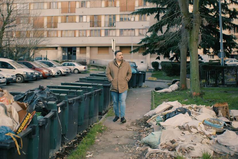 Sinan Can loopt op stoep naast afvalcontainer
