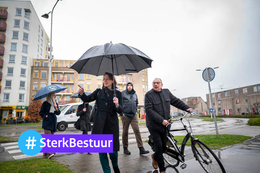 Vijf mensen lopen door de regen met paraplu en fiets aan de hand