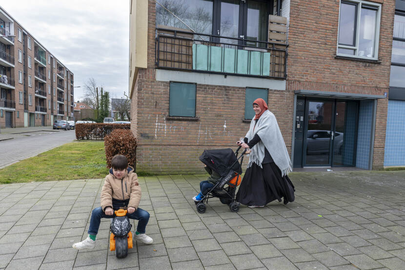 Een spelend kind en een moeder met kinderwagen vlakbij een flat