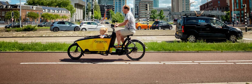 Een bakfietser op het fietspad met de weg en de skyline in de achtergrond