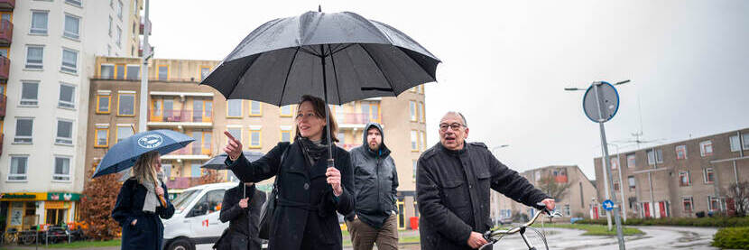 Vijf mensen lopen door de regen met paraplu en fiets aan de hand